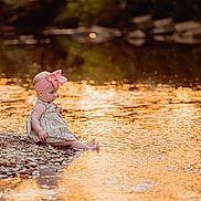Saylor joined the competition — help win amazing prizes! baby, child, girl, headband, pink_bow, dress, rocks, water, river, sunset, reflection, outdoor, nature, barefoot, sitting, curious, portrait, golden_hour, sparkle, peaceful