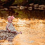 baby, child, girl, headband, pink_bow, dress, rocks, water, river, sunset, reflection, outdoor, nature, barefoot, sitting, curious, portrait, golden_hour, sparkle, peaceful