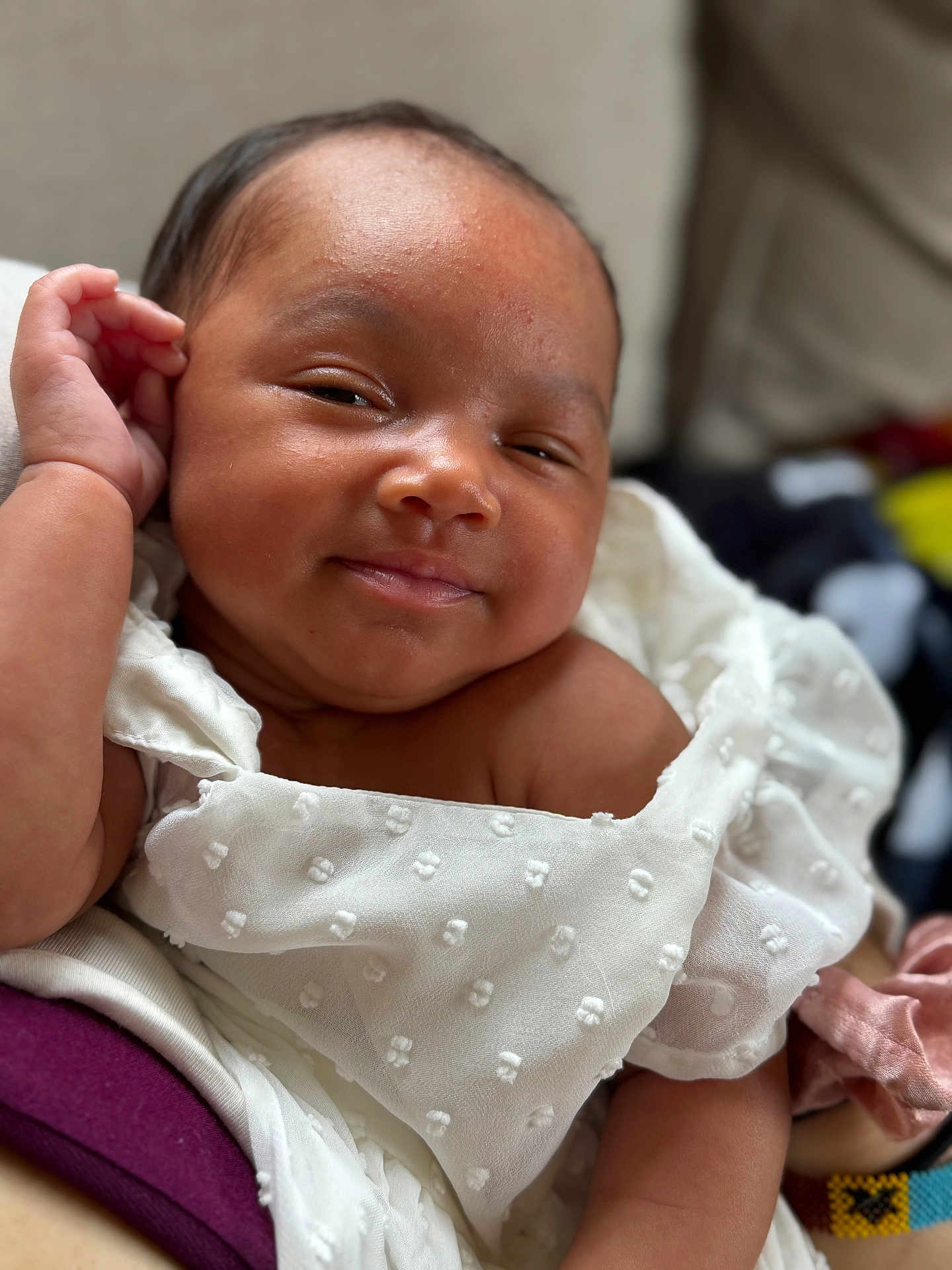 Lael is registered to the contest to win money with this photo: baby, infant, close_up, face, smile, white_clothing, textured_fabric, arm, skin, portrait, cute, child, newborn, happy, indoors, soft_light, relaxed, person, expression, head