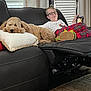 Lucky joined the competition — help win amazing prizes! dog, boy, couch, pillow, glasses, window_blinds, curtain, plaid_pants, slippers, device, living_room, black_leather, carpet, relaxing, indoor, pet, child, smile, casual, home