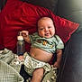 Grayson joined the competition — help win amazing prizes! baby, infant, bottle, couch, red_pillow, green_clothing, smiling, tongue_out, blanket, cozy, indoor, cute, chubby_cheeks, relaxed, child, person, portrait, happy, sitting, home