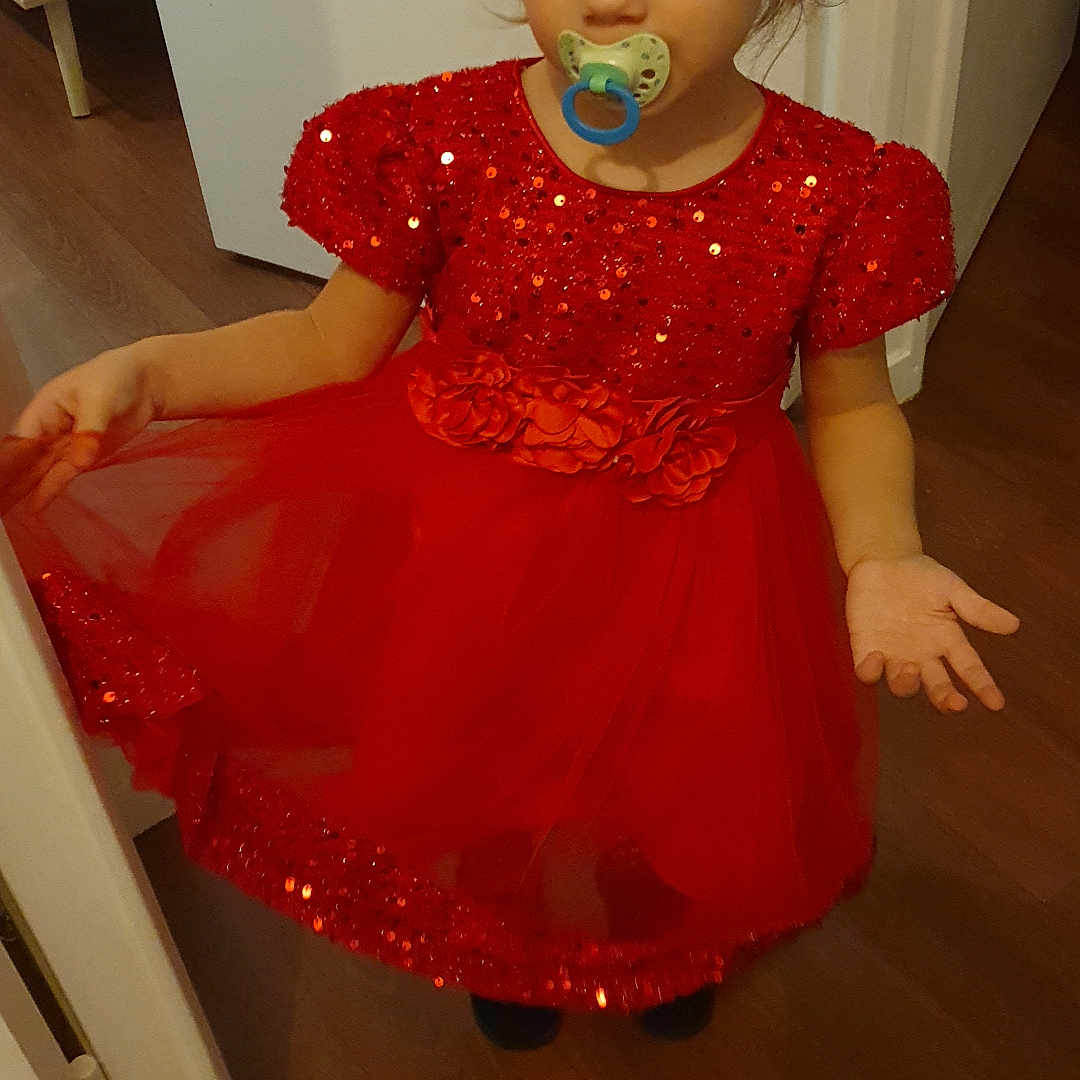 Siloë a rejoint le concours — aidez-le/la à gagner de superbes lots ! child, clothing, curly_hair, cute, door, expression, face, floor, flowers, girl, head, indoor, pacifier, person, pose, red_dress, sequins, standing, tulle, young_child