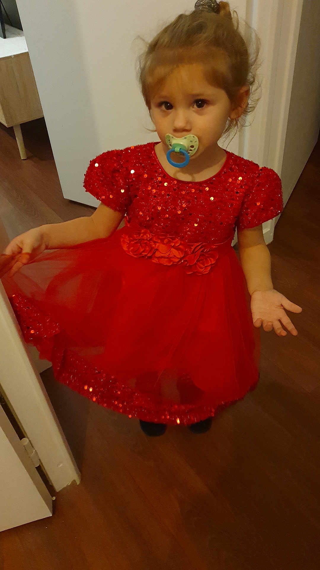 Siloë a rejoint le concours — aidez-le/la à gagner de superbes lots ! child, girl, red_dress, pacifier, indoor, floor, door, curly_hair, standing, pose, sequins, tulle, flowers, expression, young_child, cute, person, head, face, clothing
