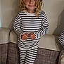 Siloë a rejoint le concours — aidez-le/la à gagner de superbes lots ! child, blonde_hair, curly_hair, striped_clothing, pajamas, indoor, couch, sofa, smiling, person, young_child, cozy, home, furniture, portrait, cute, standing, casual, comfortable, happy