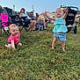 toddler, child, grass, outdoor, people, smile, crawling, standing, chairs, adult, casual_clothing, sunlight, event, family, happy, nature, daytime, stroller, lawn, relaxation