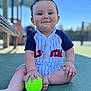 baby, child, tennis_ball, outdoor, court, sitting, cute, happy, portrait, sportswear, daylight, playful, person, infant, clothing, green, hand, foot, face, smile