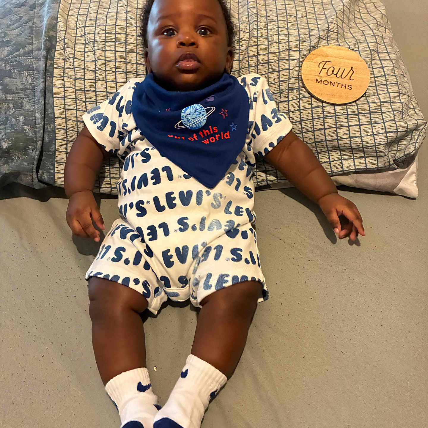 Logan joined the competition — help win amazing prizes! baby, infant, child, pillow, bed, clothing, bib, socks, levis, wooden_plaque, four_months, lying_down, indoor, person, cute, expression, face, skin, footwear, text
