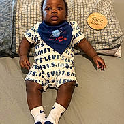 Logan joined the competition — help win amazing prizes! baby, infant, child, bed, pillow, clothing, bib, socks, levis, milestone, four_months, wooden_plaque, pattern, curly_hair, cute, alert, indoor, portrait, person, young_child