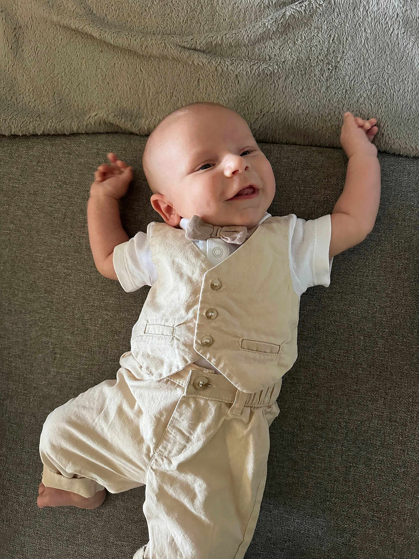 Siméo a rejoint le concours — aidez-le/la à gagner de superbes lots ! baby, infant, smiling, vest, bow_tie, white_shirt, pants, couch, fabric, relaxed, cute, portrait, indoors, person, child, happy, clothing, sitting, skin, head