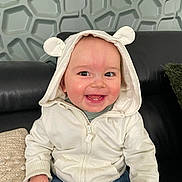 Andrea a rejoint le concours — aidez-le/la à gagner de superbes lots ! baby, hoodie, white_clothing, smiling, sitting, indoor, couch, black_leather, happy, cute, child, portrait, face, casual_wear, denim_jeans, person, modern_wall, texture, hand, hood