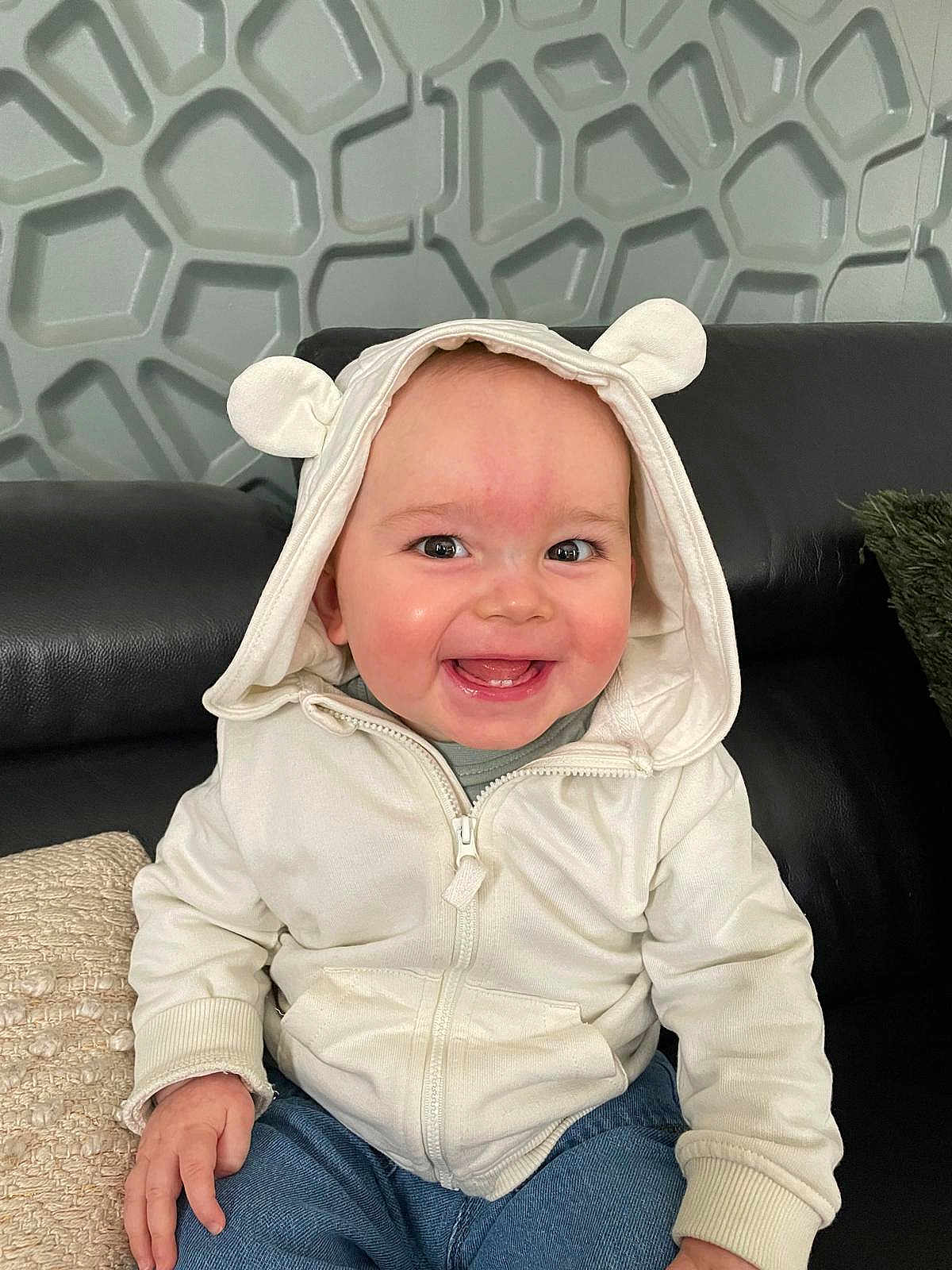 Andrea a rejoint le concours — aidez-le/la à gagner de superbes lots ! baby, hoodie, white_clothing, smiling, sitting, indoor, couch, black_leather, happy, cute, child, portrait, face, casual_wear, denim_jeans, person, modern_wall, texture, hand, hood