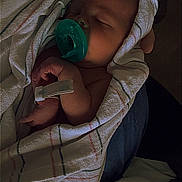 Asher is registered to the contest to win money with this photo: baby, infant, sleeping, pacifier, blanket, swaddled, portrait, face, eyes_closed, cozy, indoors, bed, bedding, relaxed, peaceful, newborn, dark_lighting, closeup, child, resting