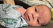 Asher is registered to the contest to win money with this photo: newborn, baby, infant, child, smiling, face, portrait, lying_down, bed, blanket, clothing, dinosaur_pattern, home, indoors, close_up, head, eyes, nose, mouth, cozy