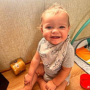 Arlo is registered to the contest to win money with this photo: baby, child, smile, sitting, floor, wooden_floor, bib, clothing, indoor, toy, red_bowl, jar, happy, cute, infant, person, face, small_teeth, home, playmat