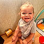 baby, child, smile, sitting, floor, wooden_floor, bib, clothing, indoor, toy, red_bowl, jar, happy, cute, infant, person, face, small_teeth, home, playmat