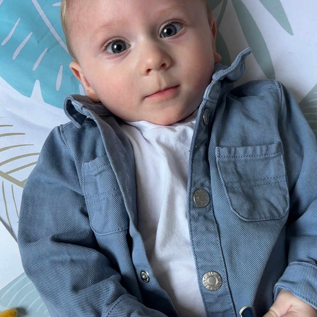 élio participe au concours pour gagner de l'argent avec cette photo : baby, blanket, blue_jacket, casual_clothing, child, curious, cute, eyes, face, hand, indoor, infant, leaf_pattern, lying_down, pattern, portrait, soft_light, stuffed_toy, white_shirt, young