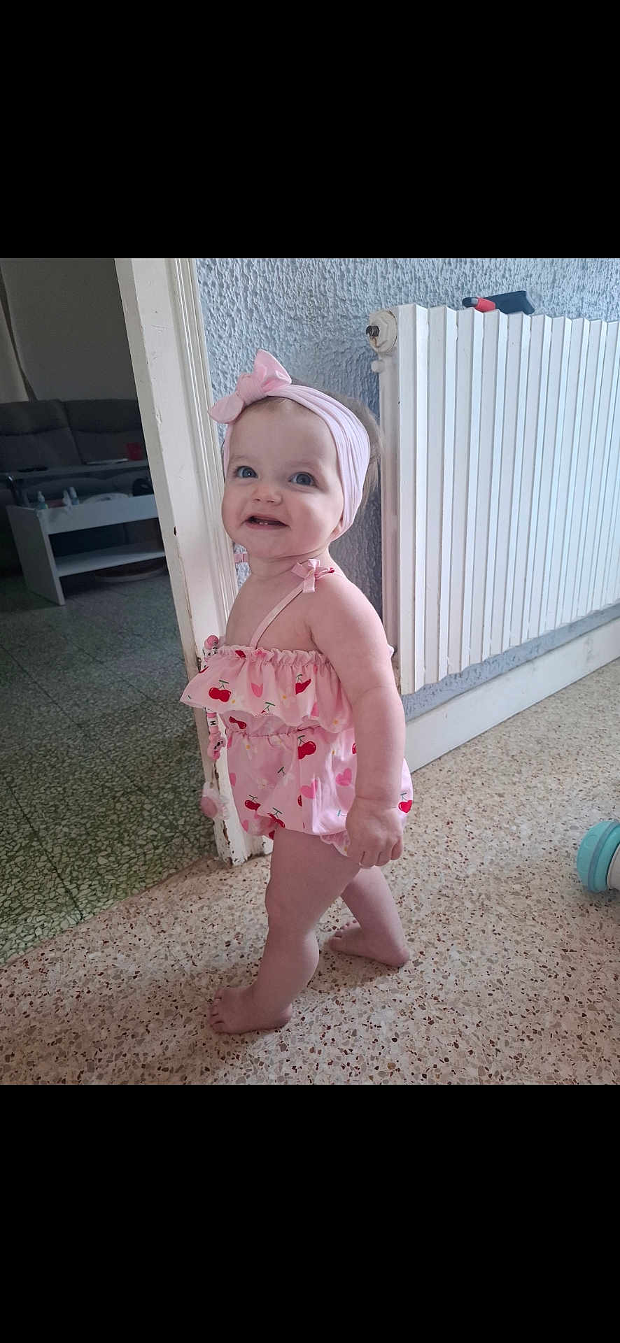 Judith participe au concours pour gagner de l'argent avec cette photo : toddler, child, barefoot, indoor, headband, pink_clothing, romper, floor, radiator, doorway, smile, happy, baby, person, home, curly_hair, standing, cheerful, cute, exploring