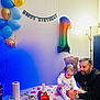 Ares participe au concours pour gagner de l'argent avec cette photo : baby, man, birthday, cake, balloons, teddy_bear, table, birthday_candle, party, number_one_balloon, banner, celebration, pajamas, indoor, lighting, food, drink, man_watching, child, family