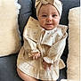 Maddison is registered to the contest to win money with this photo: baby, infant, child, smiling, headband, dress, couch, pillow, home_interior, seated, cute, portrait, indoors, cozy, soft_texture, neutral_colors, hands, legs, face, happy