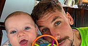 Joey is registered to the contest to win money with this photo: baby, man, toy, colorful_toy, blue_eyes, beard, green_shirt, highchair, indoor, smiling, closeup, face, portrait, family, parent, child, happy, wooden_chair, painting, window