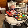 baby, sunglasses, walker, toy, book, musical_toy, shelf, basket, diapers, carpet, wooden_wall, room, indoor, baby_clothing, infant, child, face, head, seat, colorful