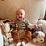 baby, infant, two_months, plush_toys, stuffed_animals, armchair, cozy, child, smiling, milestone, sign, clothing, socks, happy, indoors, portrait, cute, comfortable, seated, soft_texture