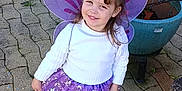 Louna participe au concours pour gagner de l'argent avec cette photo : boots, child, cobblestone_path, confetti, cute, fairy_costume, flowers_in_hair, garden, girl, hair_buns, outdoor, playful, portrait, potted_plants, purple_skirt, purple_wings, smiling, stars, white_sweater, young_person