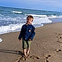 barefoot, beach, boy, child, cloudy_sky, coast, denim_jacket, footprints, ocean, outdoor, pier, playful, sand, shore, shorts, sky, smile, sunlight, water, waves