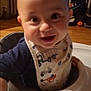 baby, child, high_chair, bib, smiling, indoor, face, hand, wooden_floor, radiator, window, toy, clothing, person, young_child, curious, happy, infant, home, portrait