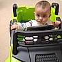 baby, child, toy_car, indoor, car, green, car_seat, steering_wheel, floor, carpet, person, infant, hand, clothing, sitting, expression, room, hallway, doorway, looking