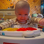 Cayde is registered to the contest to win money with this photo: baby, child, toy, skip_hop, indoor, wooden_wall, play, infant, smiling, cute, clothing, furniture, activity_center, happy, person, head, face, colorful, reaching, carpet