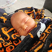 Silas is registered to the contest to win money with this photo: newborn, baby, sleeping, infant, face, portrait, blanket, wrapped, cozy, indoors, peaceful, resting, closed_eyes, nose, mouth, head, soft_fabric, orange, black, candid