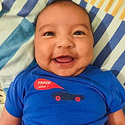 Ethan a rejoint le concours — aidez-le/la à gagner de superbes lots ! baby, infant, smiling, blue_shirt, car_graphic, blanket, striped_pattern, bed, happy, chubby_cheeks, face, eyes, tongue, mouth, lying_down, closeup, skin, person, clothing, portrait