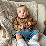 Adam a rejoint le concours — aidez-le/la à gagner de superbes lots ! baby, child, blue_eyes, brown_sweater, denim_shorts, white_socks, white_sneakers, pacifier_clip, fluffy_blanket, beige_blanket, chair, indoor, portrait, cute, curious_expression, seated, cozy, soft_texture, casual_clothing, young_child