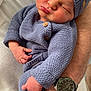 baby, sleeping, knitted_clothing, blue_hat, blue_outfit, infant, adult_arm, watch, white_sweater, close_up, peaceful, cozy, hand, portrait, indoor, skin, cute, newborn, resting, tender_moment