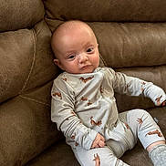 Hudson joined the competition — help win amazing prizes! baby, infant, pajamas, dog_pattern, couch, leather, brown, sitting, indoor, child, person, cute, expression, cozy, comfortable, clothing, footwear, socks, portrait, relaxed