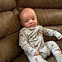 baby, infant, pajamas, dog_pattern, couch, leather, brown, sitting, indoor, child, person, cute, expression, cozy, comfortable, clothing, footwear, socks, portrait, relaxed