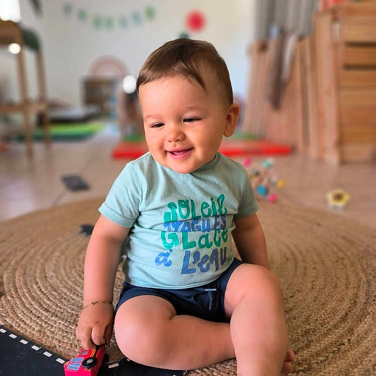 Dario participe au concours pour gagner de l'argent avec cette photo : casual_clothing, child, child_playing, cross_legged, floor, happy, home, indoor, light, person, play, room, rug, shorts, smiling, toddler, toy_car, tshirt, wooden_furniture, young_child