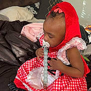 Delijah is registered to the contest to win money with this photo: toddler, child, baby, red_hood, pacifier, bed, blanket, pillow, dress, checkered_pattern, indoors, skin, barefoot, sitting, clothing, headwear, infant, cute, young_child, portrait