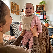 Louise a rejoint le concours — aidez-le/la à gagner de superbes lots ! baby, child, adult, holding, living_room, plant, bookshelf, bib, pink_clothing, smile, cozy, home_interior, person, furniture, socks, happy, indoor, portrait, family, care