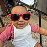 baby, child, sunglasses, red, white_overalls, striped_shirt, smiling, outdoor, residential_area, person, lap, sunlight, happy, face, head, arm, legs, rocks, tree, stairs