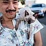 Charlotte joined the competition — help win amazing prizes! man, person, cat, siamese_cat, blue_eyes, shoulder, floral_shirt, smile, facial_hair, outdoor, daylight, urban, sidewalk, vehicle, necklace, happy, young_adult, closeup, pet, animal