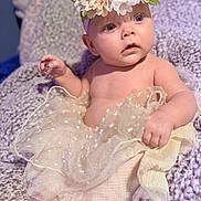 Piper joined the competition — help win amazing prizes! baby, infant, child, portrait, flower_crown, floral_headband, dress, tulle, sparkly_fabric, blanket, sitting, wide_eyed, looking_at_camera, barefoot, toes, hand, cozy, indoor, soft_lighting, close_up