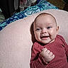 baby, infant, child, smiling, happy, portrait, face, blue_eyes, lying_down, blanket, pink_blanket, red_clothing, long_sleeves, hand, indoor, home, bed, bedding, close_up, candid