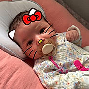 Isabella is registered to the contest to win money with this photo: baby, infant, pacifier, pink, cushion, onesie, floral_pattern, face_filter, hello_kitty, whiskers, bow, cute, lying_down, indoors, soft_toys, child, sleeping_bed, baby_accessories, playful, closeup