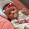baby, infant, pacifier, pink, cushion, onesie, floral_pattern, face_filter, hello_kitty, whiskers, bow, cute, lying_down, indoors, soft_toys, child, sleeping_bed, baby_accessories, playful, closeup