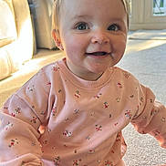 Ivy is registered to the contest to win money with this photo: baby, child, smiling, pink_clothing, floral_pattern, sitting, carpet, indoor, natural_light, sunlight, window, happy, cute, person, young_child, casual_wear, home_interior, cozy, portrait, candid