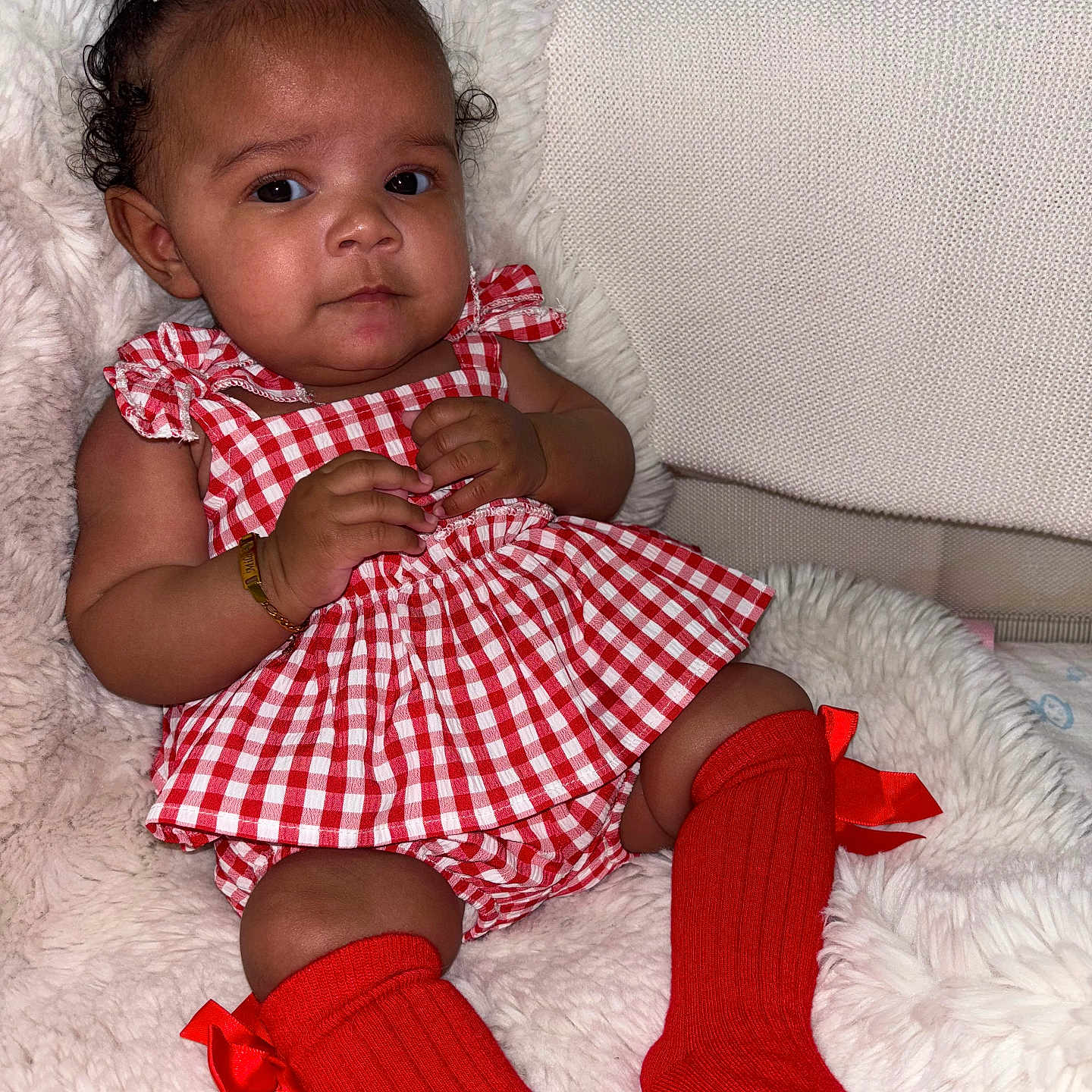 Mila Abbott joined the competition — help win amazing prizes! baby, bows, bracelet, checkered_pattern, child, curly_hair, cute, dress, face, fluffy_cushion, footwear, hands, indoor, infant, legs, portrait, red_socks, seated, smiling, white_bows
