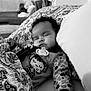 baby, sleeping, pacifier, blanket, pillow, bed, curly_hair, infant, indoor, cozy, patterned_clothing, monochrome, soft_lighting, child, peaceful, cute, resting, comfort, nursery, plush_toys