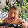 Amir is registered to the contest to win money with this photo: toddler, child, smiling, happy, outdoor, brick_wall, bicycle, greenery, hand, face, person, playful, daylight, bare_chest, wicker, pavement, garden, toy, nature, expression